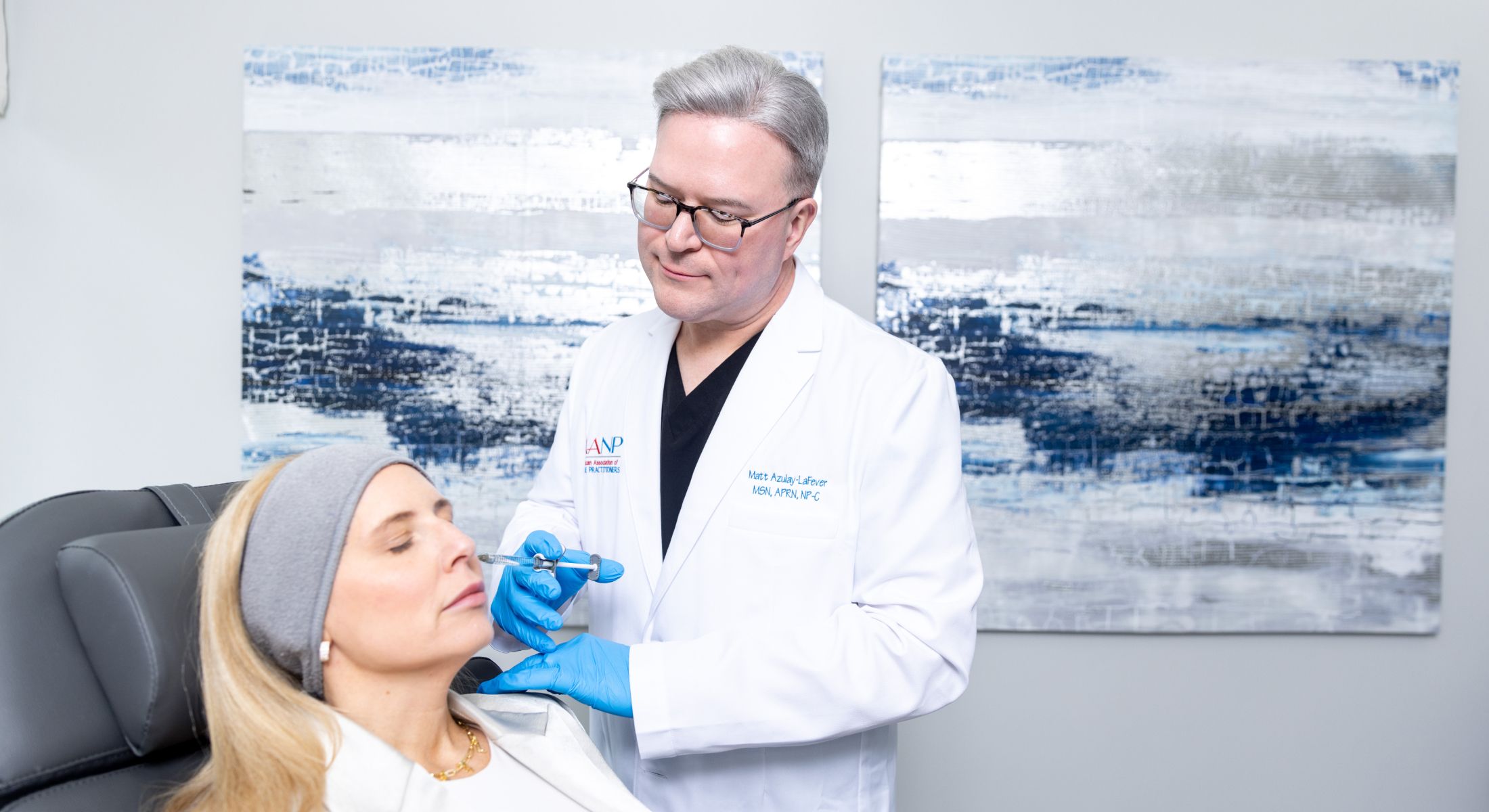 matt azulay-lafever in a white doctors coat injecting a patient model with an injectable