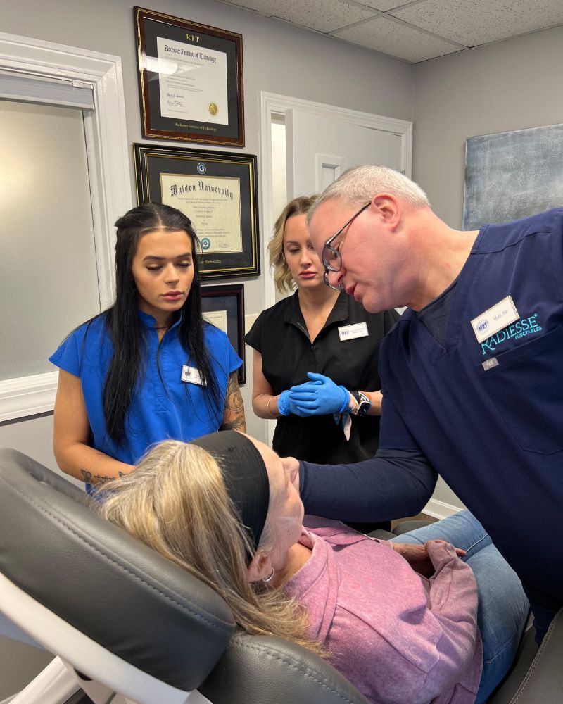 Matt Azulay-LaFever with two students and a patient model sitting in a med spa chair