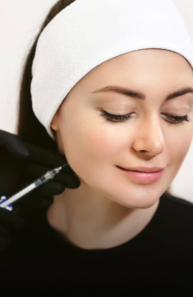 aesthetic training student injecting filler into a patient model's jaw